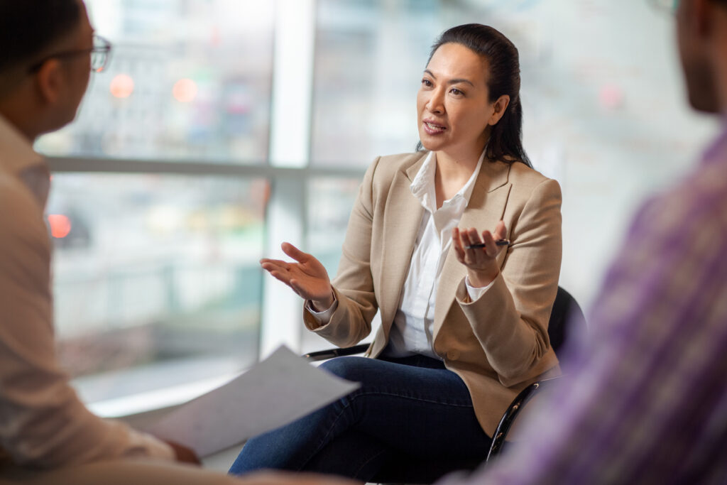 Multiracial Asian Hispanic Pacific Islander mature woman talking with colleagues in business office in meeting